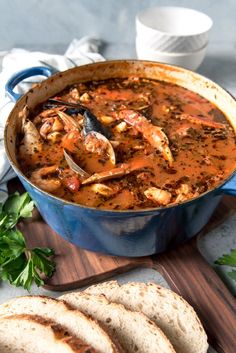 a blue pot filled with food next to sliced bread on top of a wooden cutting board