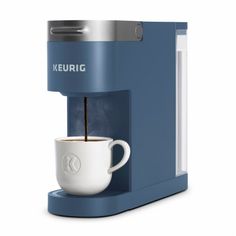 a blue keurig coffee maker with a white cup filled with liquid and steam coming out of it