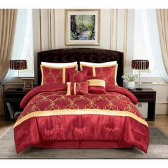 a bed with red and gold comforter set in a living room next to a window