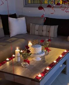 a table topped with a cake and candles next to a couch covered in red roses