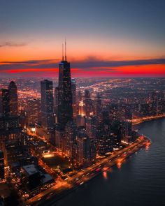 an aerial view of the city lights and skyscrapers at night, with water in the foreground