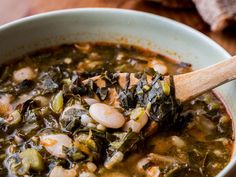 a wooden spoon in a bowl filled with stew and greens on top of a table