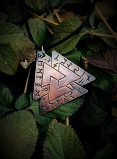 a triangle shaped pendant is sitting on some leafy branches and has writing in the middle