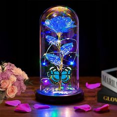 a blue flower under a glass dome on a wooden table with pink flowers in the background