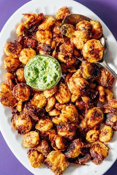 a white plate topped with fried chicken next to a green sauce