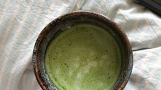 a green drink in a brown bowl on a white blanket next to a laptop computer