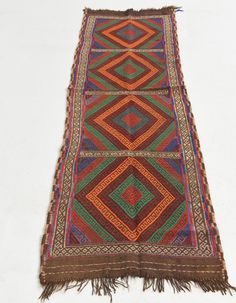 an old multicolored rug with fringes on the bottom and sides, sitting on a white surface