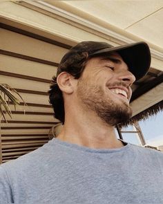 a man wearing a hat and smiling for the camera with his eyes closed, standing in front of a house