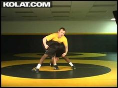 two men are wrestling on a black and yellow mat in an indoor gym with the words kolat com above them