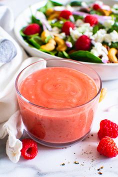 a bowl of salad with raspberries next to it