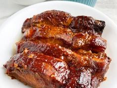 ribs covered in bbq sauce on a white plate next to a cup of coffee