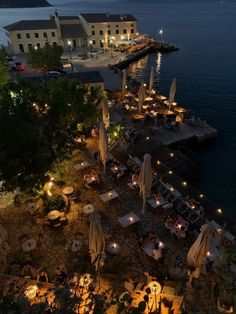 an outdoor dining area next to the water at night with lit up tables and umbrellas