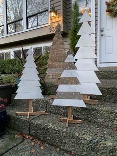 three wooden christmas trees are sitting on the steps in front of a house with potted plants