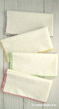 three white place mats with green, yellow and red scalloped edges on a wooden surface