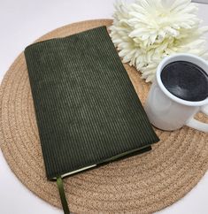 a cup of coffee next to a book on a mat with a flower in the background