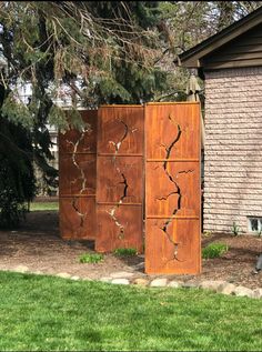 three wooden boxes sitting in the grass next to a brick wall and tree branch covered building