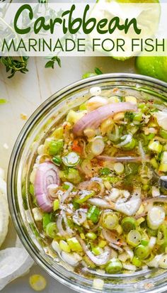 a glass bowl filled with vegetables on top of a white table next to limes