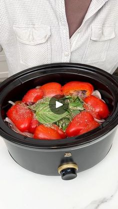 a person holding a black crock pot filled with tomatoes and spinach in it