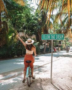 a woman riding a bike next to a green street sign that says follow that dream