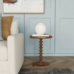 a white vase sitting on top of a wooden table next to a couch in a living room