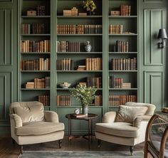 two chairs and a table in front of bookshelves with green paint on the walls