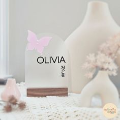 a white vase with a pink butterfly on it sitting next to an object that says oliva