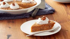 a slice of pumpkin pie on a white plate with a fork and bowl in the background