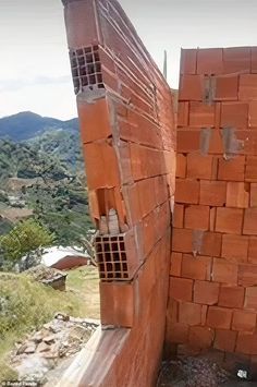 a red brick wall with holes in the middle and mountains in the backround