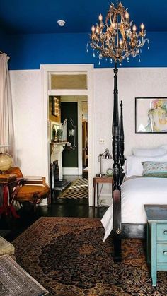 a bedroom with blue walls and white bedding has a chandelier hanging from the ceiling