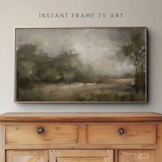 a large painting hanging on the wall above a wooden dresser with drawers underneath it and an inscription that reads instant frame tv art