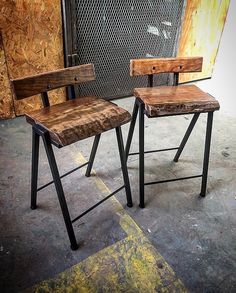 two wooden chairs sitting next to each other in front of a metal fence and wall