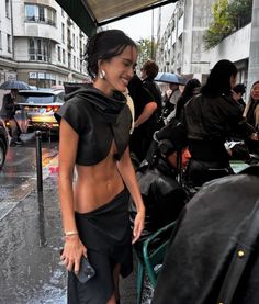 a woman is standing in the rain with an umbrella over her head and wearing a skirt