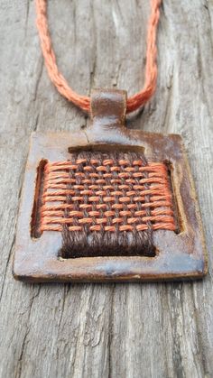 an orange and brown piece of wire on a wooden surface with a square pendant attached to it