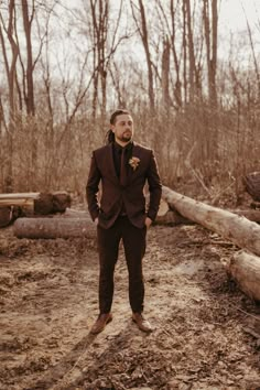 a man wearing a suit and tie standing in front of some logs on the ground