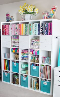 a white bookcase filled with lots of colorful books next to a vase full of flowers