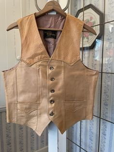 "This vest is made of very soft leather in two tones of light tan brown. It has the original buttons in the front and two front pockets. The front and back yokes and pockets are trimmed with matching braided leather. The vest is fully lined with light brown acetate lining. The label reads \"Le Cuir Niko Leather.\" The measurements, taken with the vest lying flat, are: shoulder to shoulder, 13 1/2 inches; armpit to armpit, 22 inches; length, 25 inches in front and 21 inches in back; bottom edge, 22 inches. Please note that there are some spots on the right front; otherwise, the vest is in very good condition." Cowboy Shoot, Brown Leather Vest, Cowboy Vest, Vintage Leather Vest, Western Vest, Leather Waistcoat, Jacket Ideas, Bad Batch, Vest Outfits