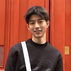 a young man standing in front of a red door with a white bag on his shoulder