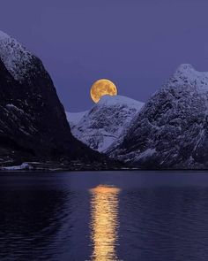 the full moon is reflected in the still water of a lake with snow covered mountains behind it