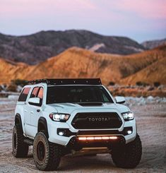 a white toyota truck parked on top of a dirt field in front of some mountains