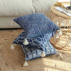 two blue and white pillows stacked on top of each other in front of a couch