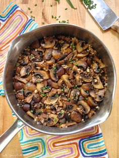 a pan filled with mushrooms and peas on top of a wooden table next to utensils