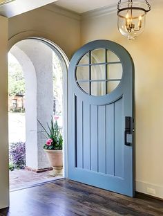 a blue front door with an arched glass window and potted plant on the side