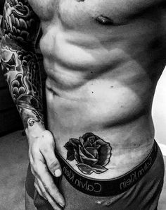 a man with a rose tattoo on his chest and lower half is standing in front of a mirror