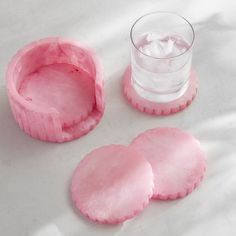 three pieces of pink food next to a glass of water on a white tablecloth