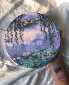 a person's hand holding up a painted plate with water lilies on it