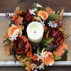 a candle is lit in the center of a wreath with flowers and leaves on it