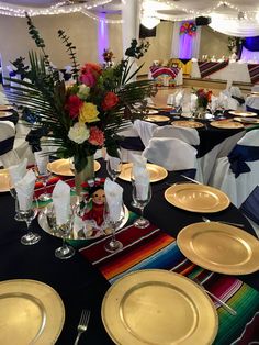 the table is set with gold plates, silverware and colorful flowers in a vase