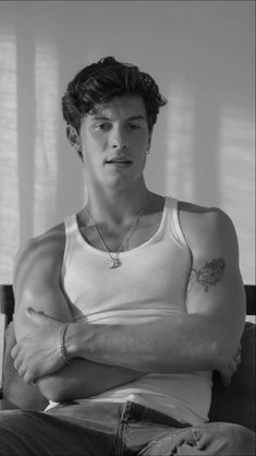 a man sitting on top of a chair wearing a white tank top and holding his arms crossed