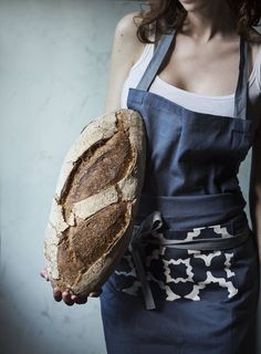 a woman holding a loaf of bread in her hand and wearing an apron on the other side