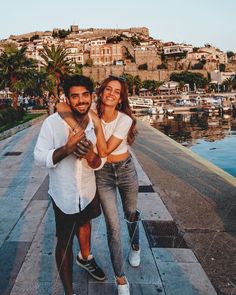 a man and woman standing next to each other on a pier with boats in the background